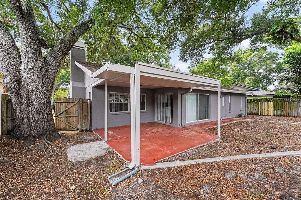 A gray house with a covered red patio and a large tree in the backyard — 2431 GROVE RIDGE DRIVE, PALM HARBOR, FL