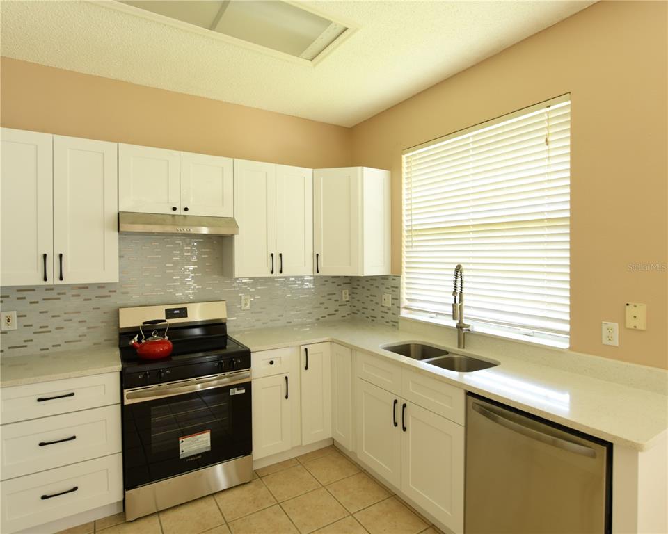 A kitchen with white cabinets, stainless steel appliances, a tiled backsplash, and a window — 812 JADE FOREST AVENUE, ORLANDO, FL