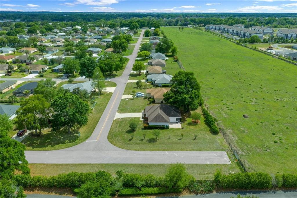 An aerial view shows a suburban street with single-family homes bordering a large grassy field — 3498 NW 50TH COURT, OCALA, FL