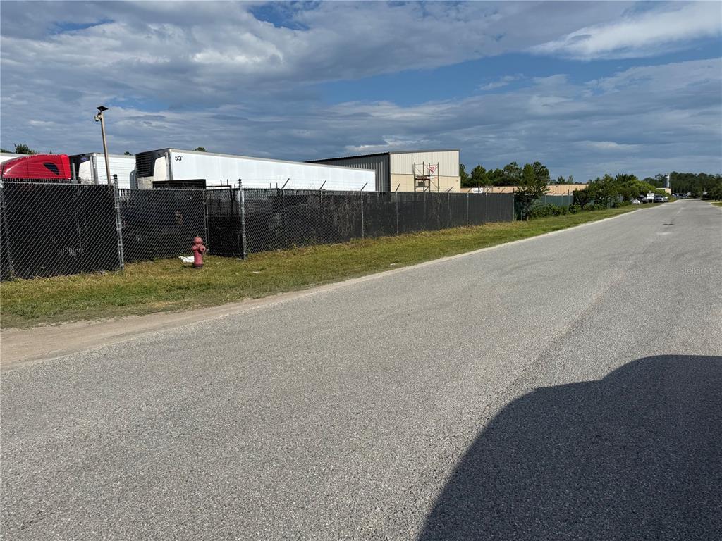 A paved road runs alongside a fenced industrial lot containing semi-trailers and a warehouse building — 3330 STEEL RAIL DR DRIVE UNIT 1, BUNNELL, FL