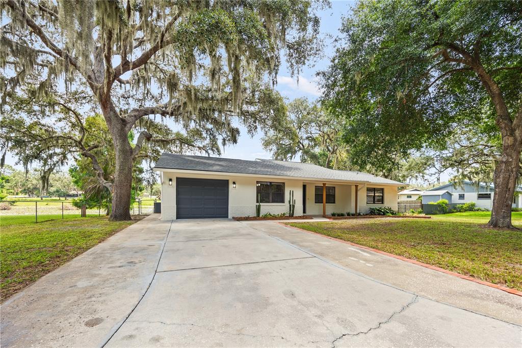 A single-story house with a gray garage door, concrete driveway, and large mossy oak trees — 2457 S SUMMERWOOD POINT, INVERNESS, FL