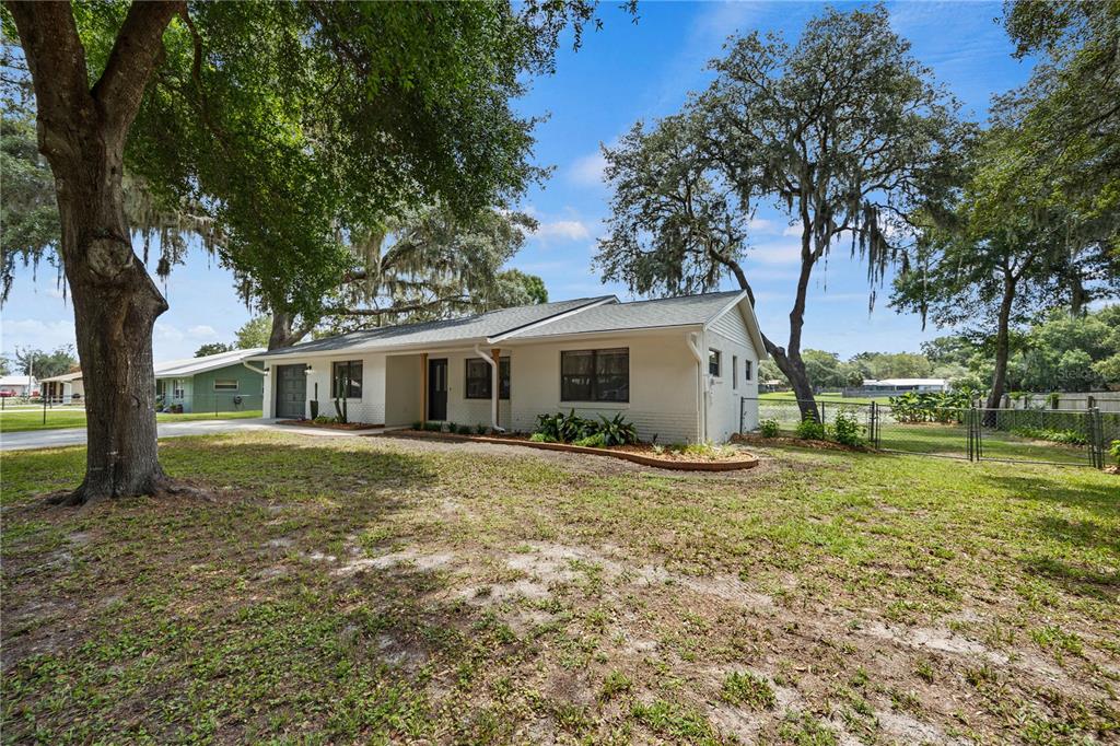 A white single-story house with a gray roof sits on a grassy lot with trees — 2457 S SUMMERWOOD POINT, INVERNESS, FL