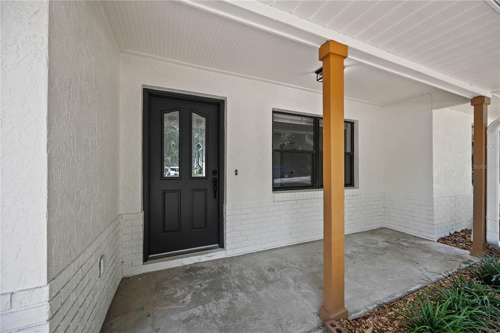 A covered front porch features a black door, white brick siding, and wooden support posts — 2457 S SUMMERWOOD POINT, INVERNESS, FL
