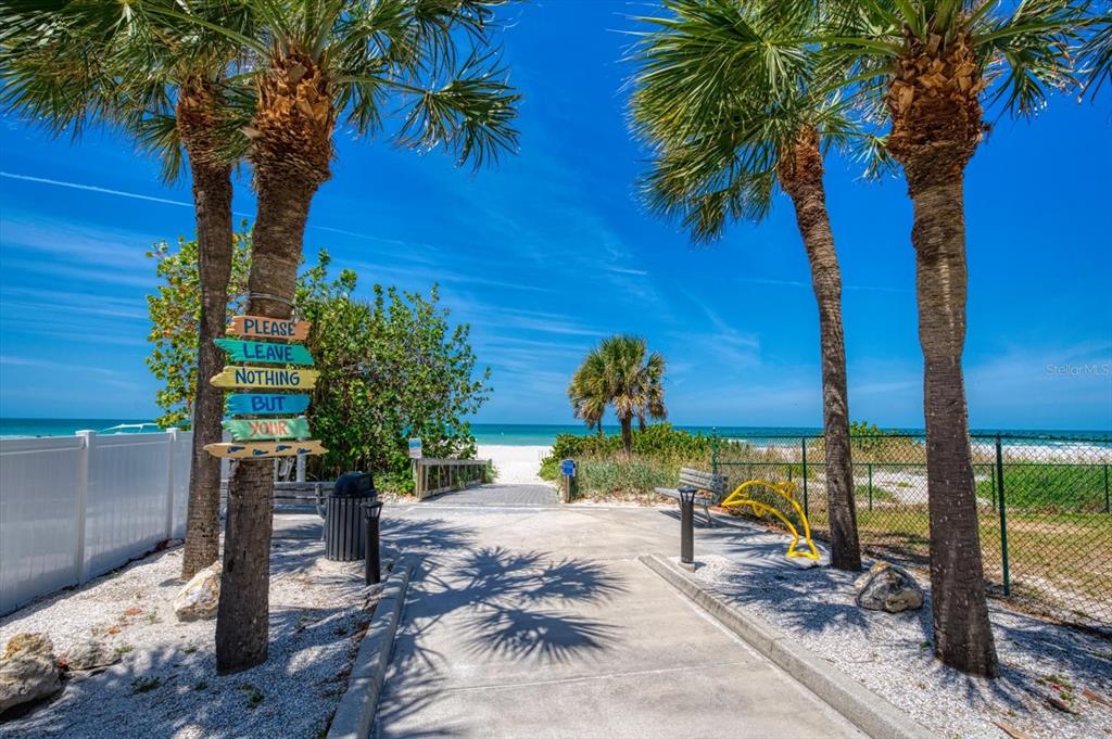 A paved walkway leads between palm trees toward a sandy beach under a clear sky — 901 HARBOUR HOUSE DRIVE, INDIAN ROCKS BEACH, FL