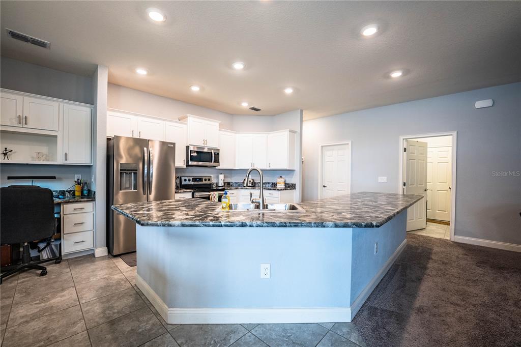 A kitchen features white cabinets, stainless steel appliances, a marble-patterned island, and tile flooring — 261 WALKERS POINT DRIVE, AUBURNDALE, FL