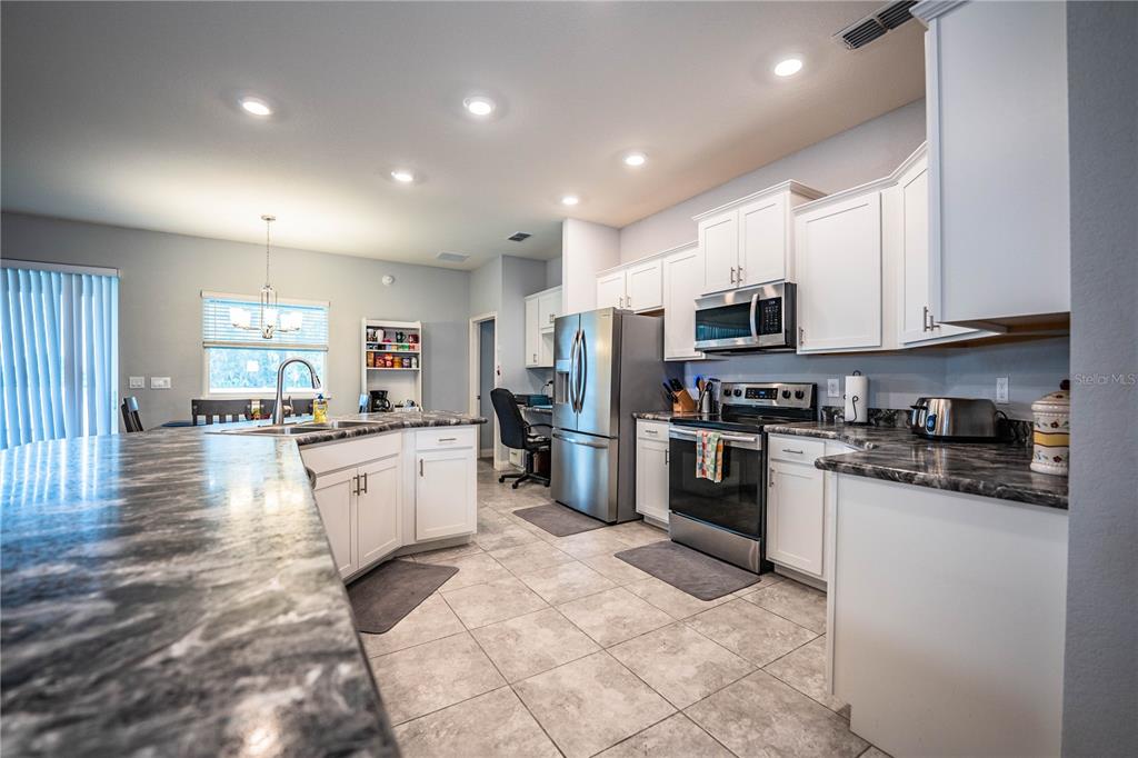 A kitchen features white cabinets, dark marble-patterned countertops, stainless steel appliances, and tile flooring — 261 WALKERS POINT DRIVE, AUBURNDALE, FL