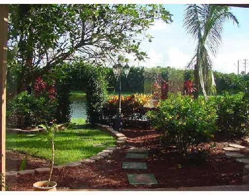 A landscaped backyard features a stone path, a garden lamp, and a view of water — 9067 Long Lake Palm Drive, Boca Raton FL 33496, BOCA RATON, FL