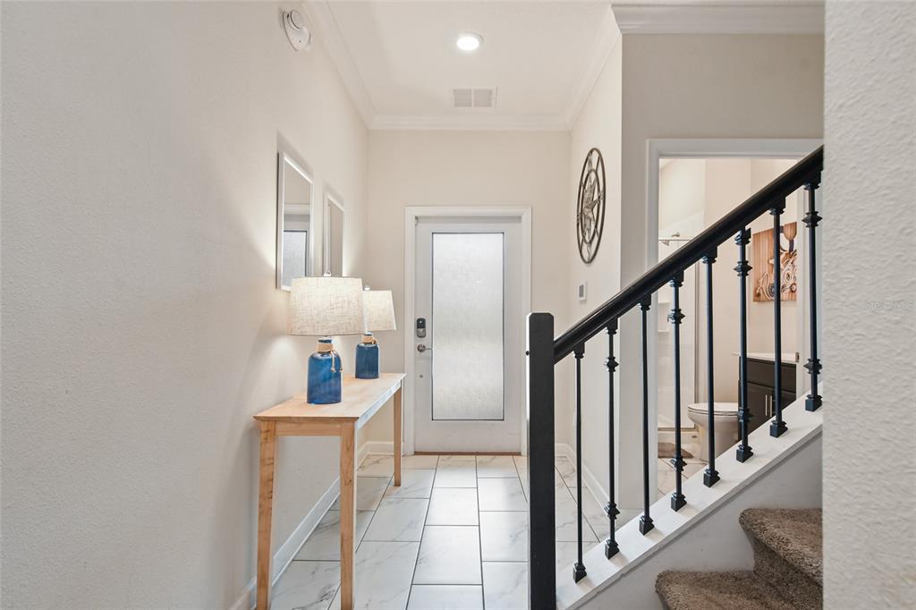 A bright entryway features a console table, blue lamps, tiled flooring, and a carpeted staircase — 1244 CHALLENGE DRIVE, DAVENPORT, FL