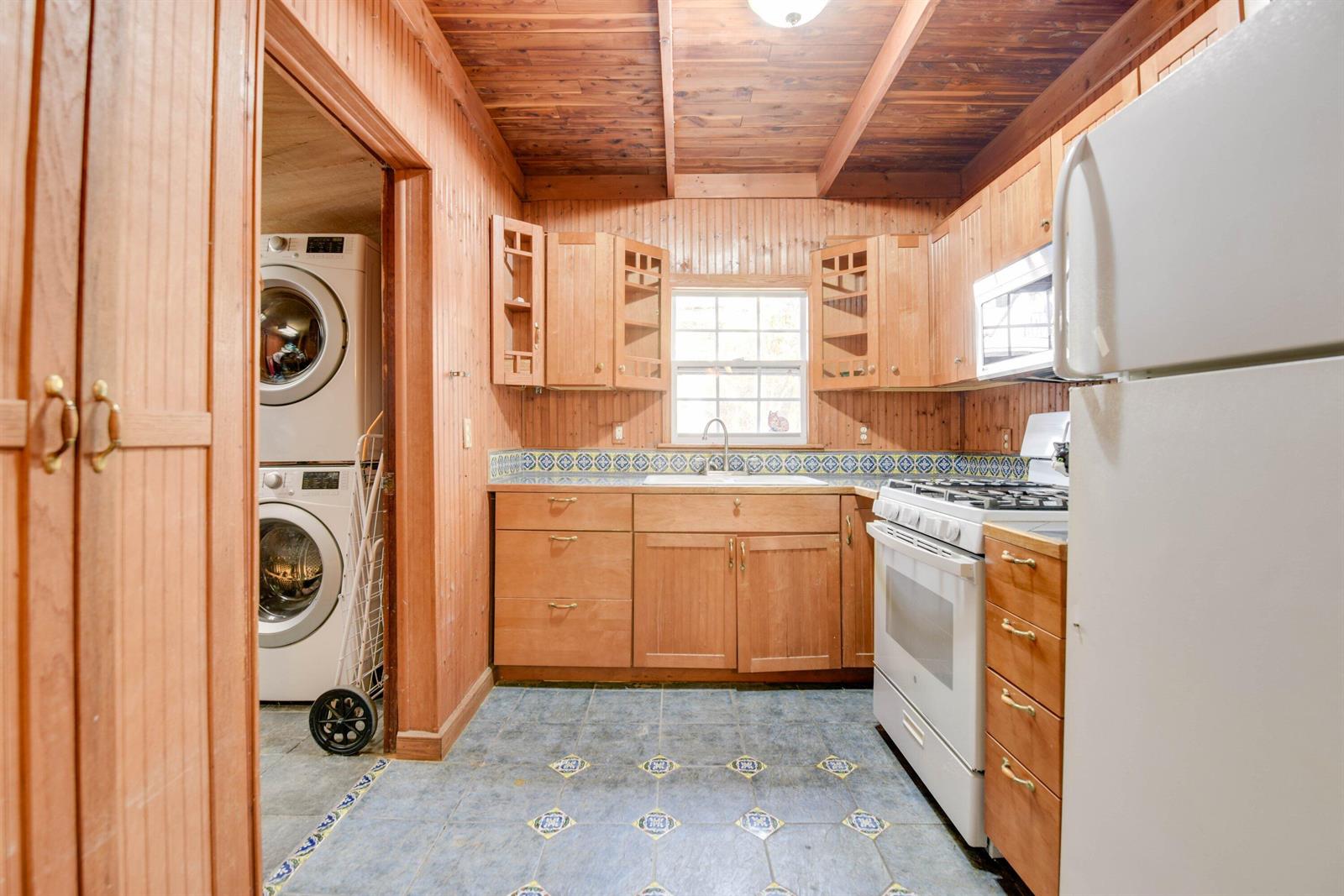 A kitchen with wood-paneled walls, tile flooring, and an adjacent laundry area with stacked appliances — 1425 Eliza Street, Key West FL 33040, KEY WEST, FL