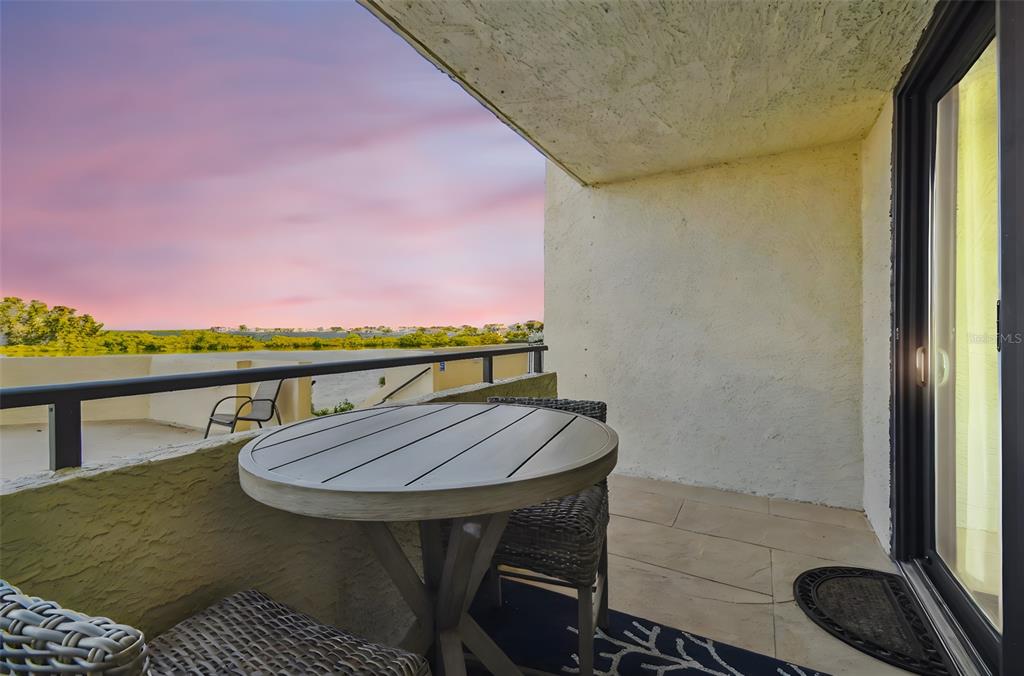 A balcony with a round table, wicker chairs, and a view of the sunset — 5915 SEA RANCH DRIVE UNIT 108, HUDSON, FL