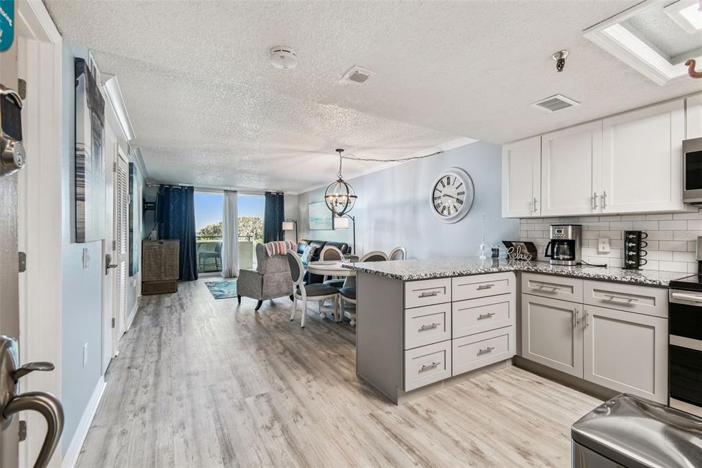 An open-concept kitchen and living area features light wood flooring, white cabinetry, and a balcony — 5915 SEA RANCH DRIVE UNIT 108, HUDSON, FL