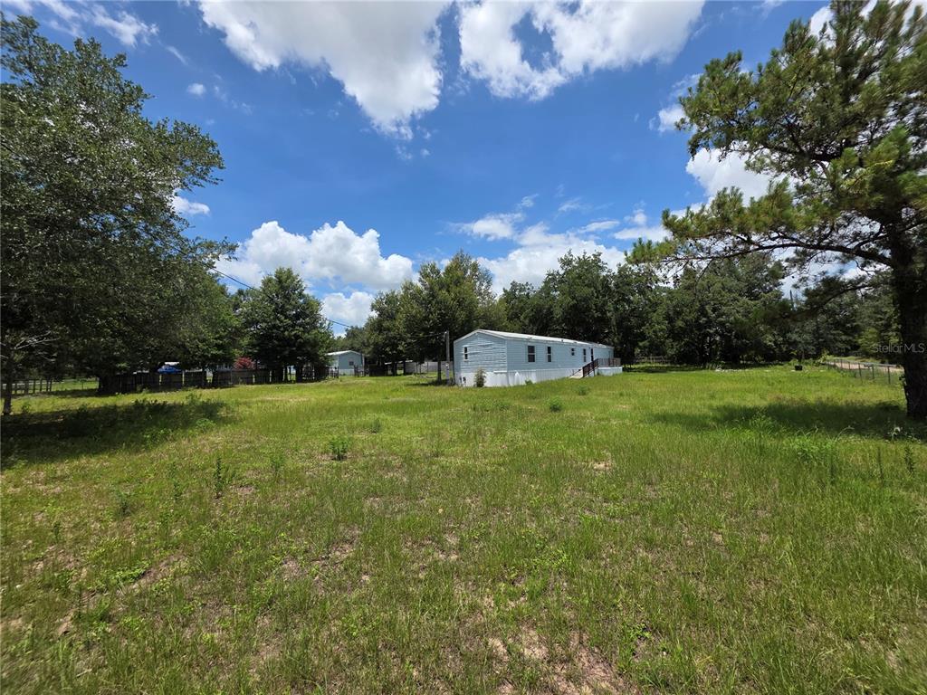 A light-colored manufactured home sits in the middle of a large, grassy, tree-lined lot — 8443 HAMSTER DRIVE, ZEPHYRHILLS, FL
