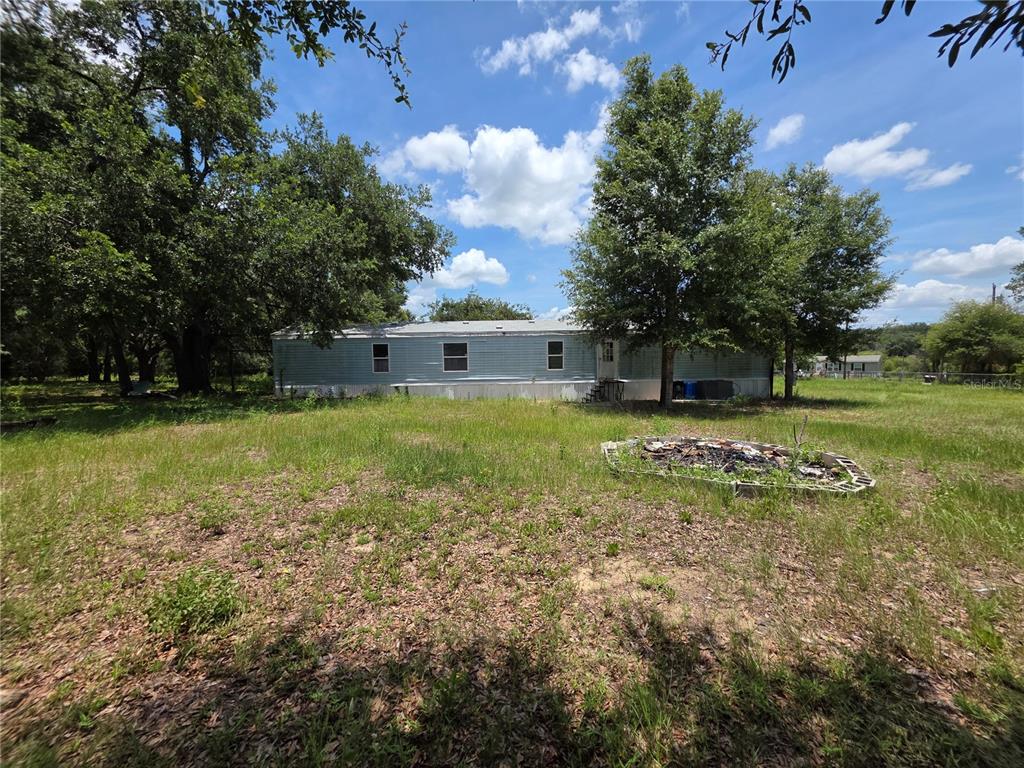 A single-story manufactured home sits on a grassy lot with trees and a fire pit — 8443 HAMSTER DRIVE, ZEPHYRHILLS, FL
