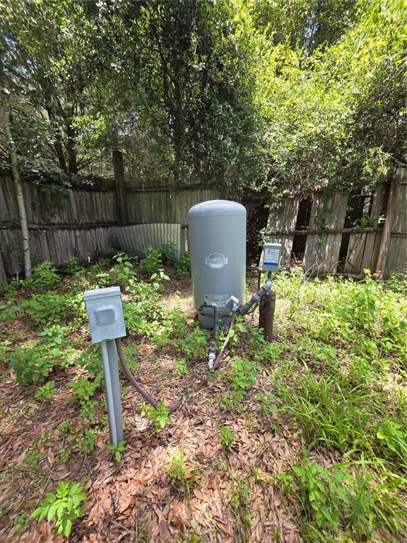 A grey water pressure tank and electrical disconnect box are located in a grassy yard — 8443 HAMSTER DRIVE, ZEPHYRHILLS, FL
