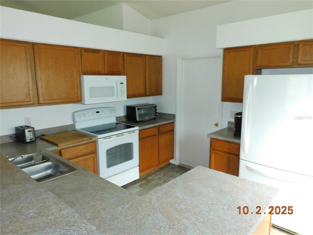 A kitchen features wood cabinets, white appliances, and gray laminate countertops — 2542 CAMPHORWOOD CIRCLE, KISSIMMEE, FL