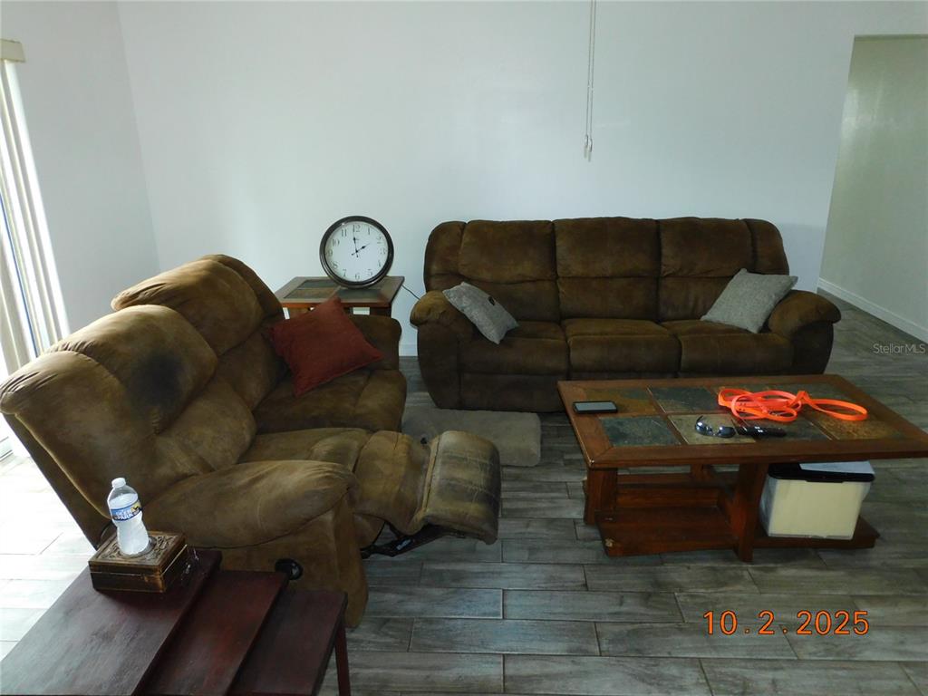 A living room features brown reclining sofas, a tiled coffee table, and wood-look tile flooring — 2542 CAMPHORWOOD CIRCLE, KISSIMMEE, FL