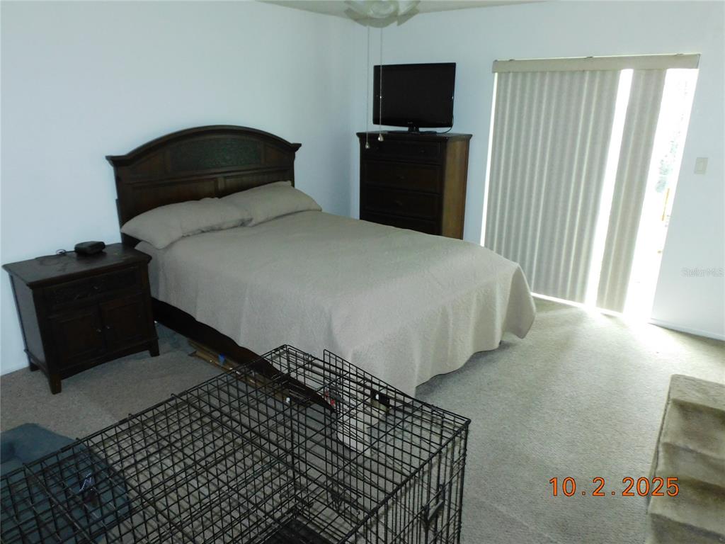 A bedroom features a bed, a dresser with a television, and a metal pet crate — 2542 CAMPHORWOOD CIRCLE, KISSIMMEE, FL