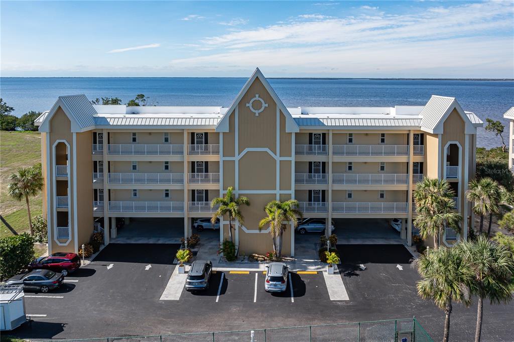 An exterior view of a three-story tan apartment building with balconies facing the water — 101 N MARION COURT UNIT 114, PUNTA GORDA, FL