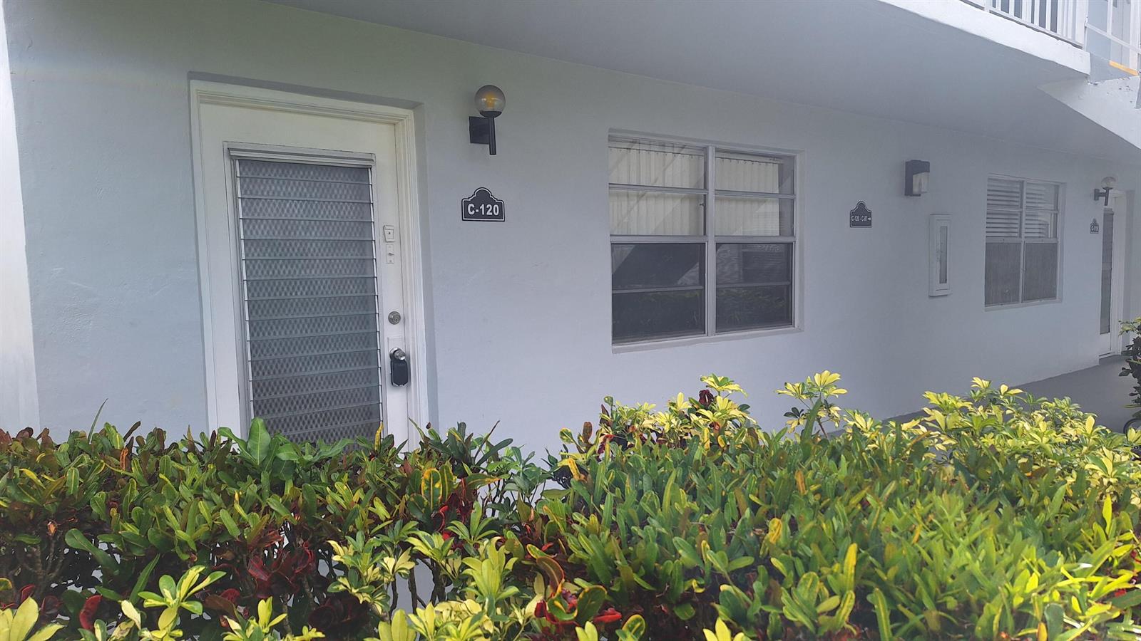 Exterior view of a ground-floor apartment unit with a white door and louvered windows — 120 Normandy # C, Delray Beach FL 33484, DELRAY BEACH, FL
