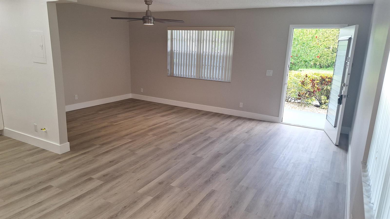 An empty living room features light wood-look flooring, gray walls, a ceiling fan, and an open door — 120 Normandy # C, Delray Beach FL 33484, DELRAY BEACH, FL