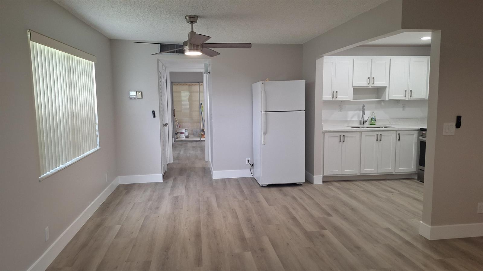 A dining area with wood-look flooring leads to a kitchen with white cabinets and appliances — 120 Normandy # C, Delray Beach FL 33484, DELRAY BEACH, FL