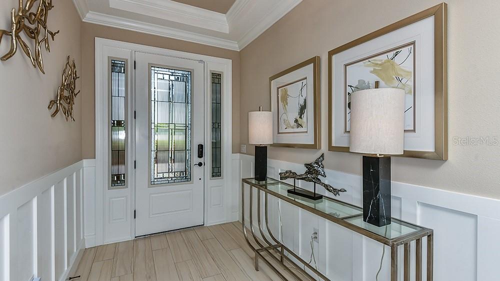 A bright entryway features a white front door, a glass console table, and wall art — 3912 MASANIELLO WAY, WESLEY CHAPEL, FL