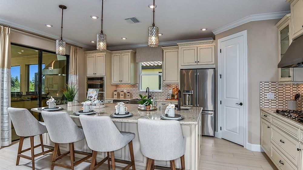 A kitchen features an island with four chairs, stainless steel appliances, and light-colored cabinetry — 3912 MASANIELLO WAY, WESLEY CHAPEL, FL