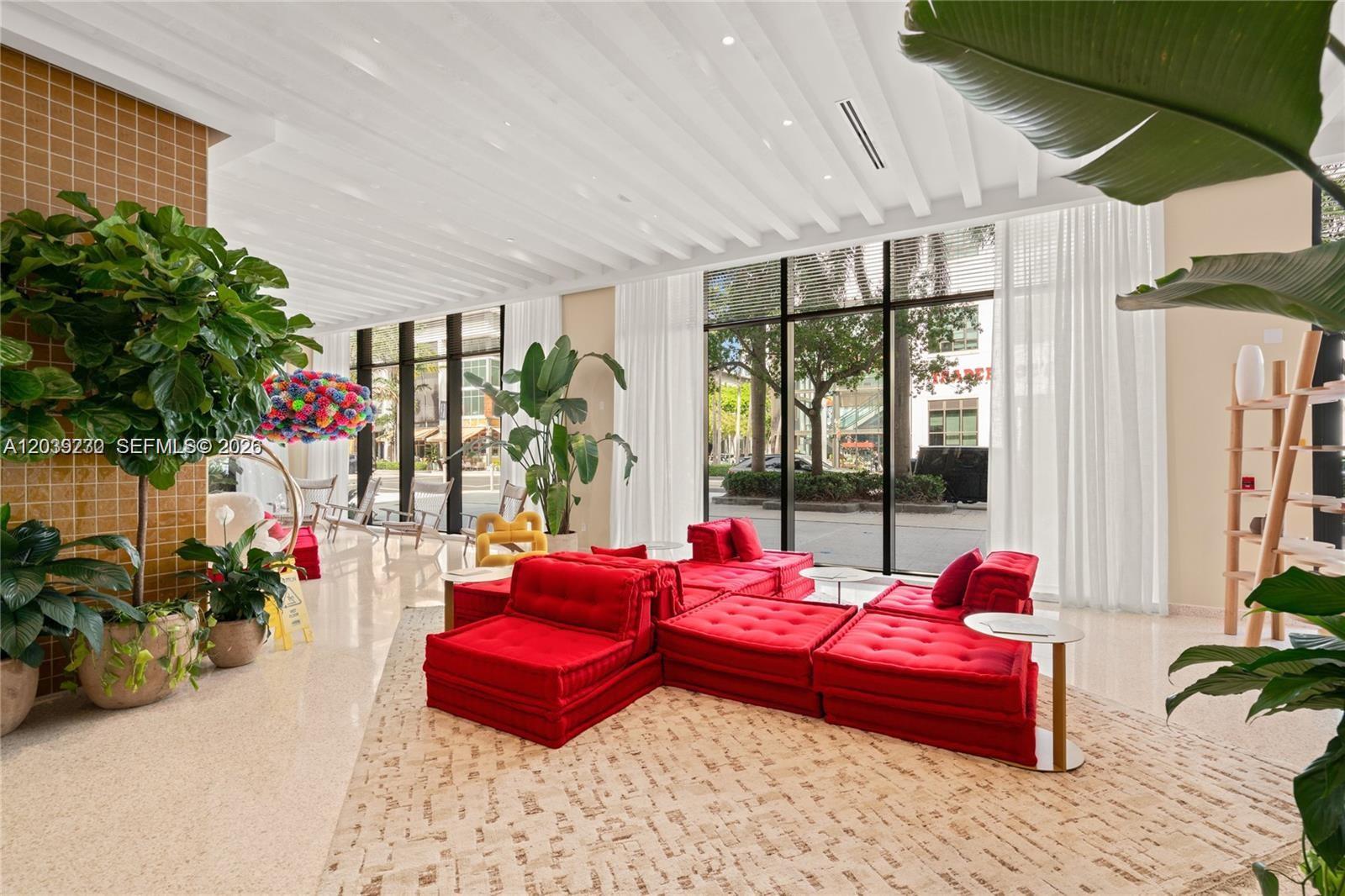 A bright lobby features red modular seating, large windows, and potted plants on a patterned rug — 90 NE 32nd St # 1009, Miami FL 33127, MIAMI, FL