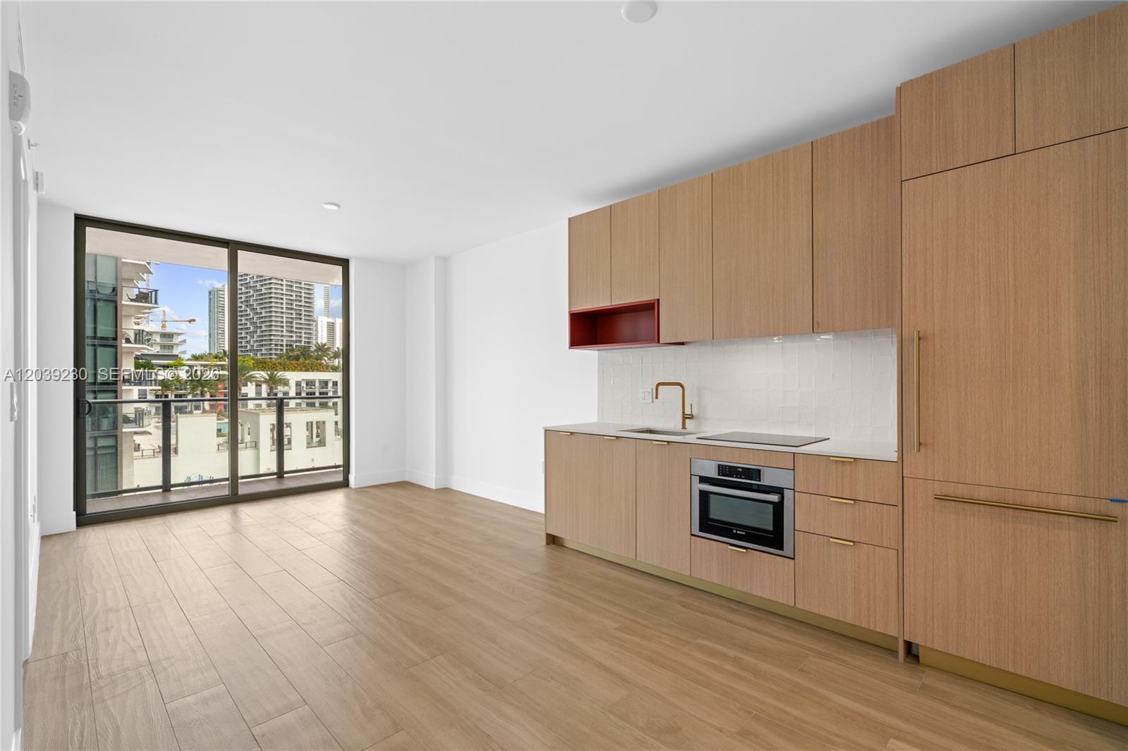 A modern kitchen features light wood cabinetry, gold hardware, and a balcony with city views — 90 NE 32nd St # 1009, Miami FL 33127, MIAMI, FL