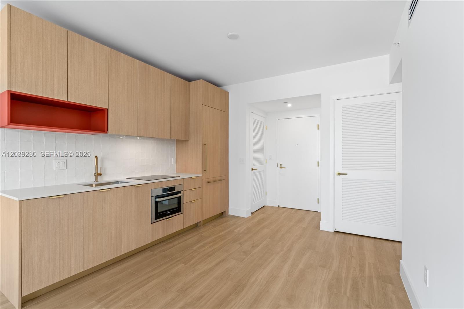 A modern kitchen features light wood cabinets, a red open shelf, and white countertops — 90 NE 32nd St # 1009, Miami FL 33127, MIAMI, FL