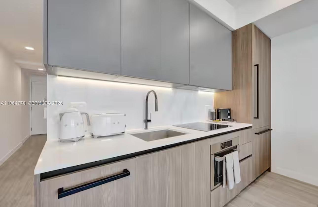 A modern kitchen features gray upper cabinets, wood-grain lower cabinets, white countertops, and integrated appliances — 580 72 # 1713, Miami Beach FL 33141, MIAMI BEACH, FL