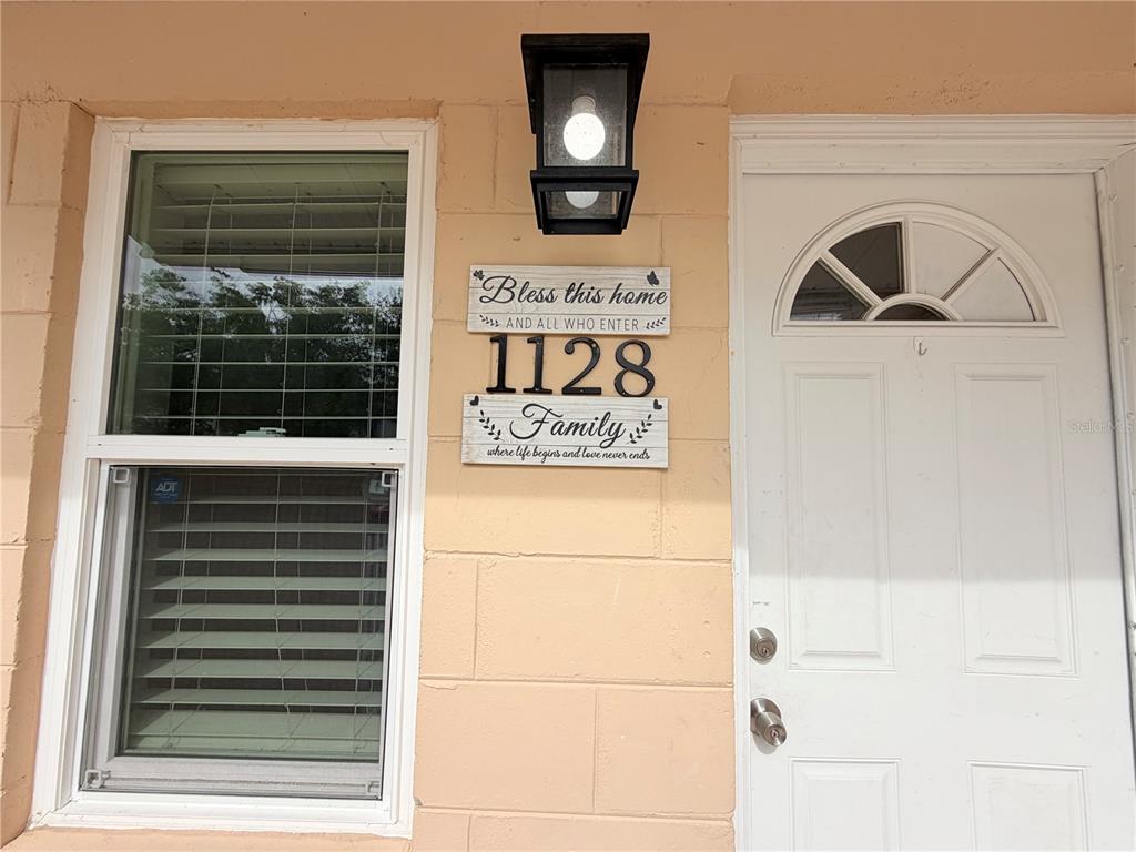 A white front door sits next to a window and a decorative address sign — 1128 SOPHIE BOULEVARD, ORLANDO, FL