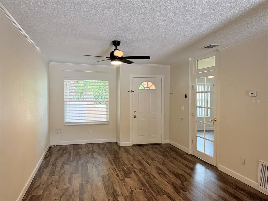 An empty room features wood-look flooring, a ceiling fan, a white front door, and glass-paned doors — 1128 SOPHIE BOULEVARD, ORLANDO, FL
