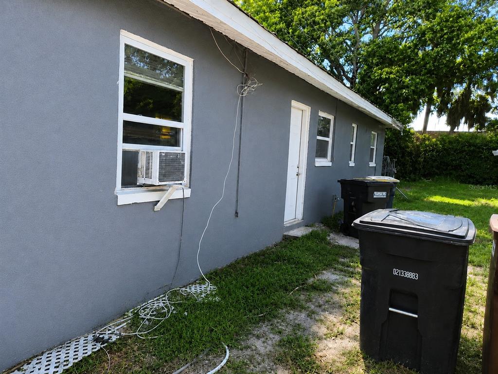 The exterior of a gray house features a window air conditioner, a door, and trash bins — 1506 N MADISON AVENUE, CLEARWATER, FL