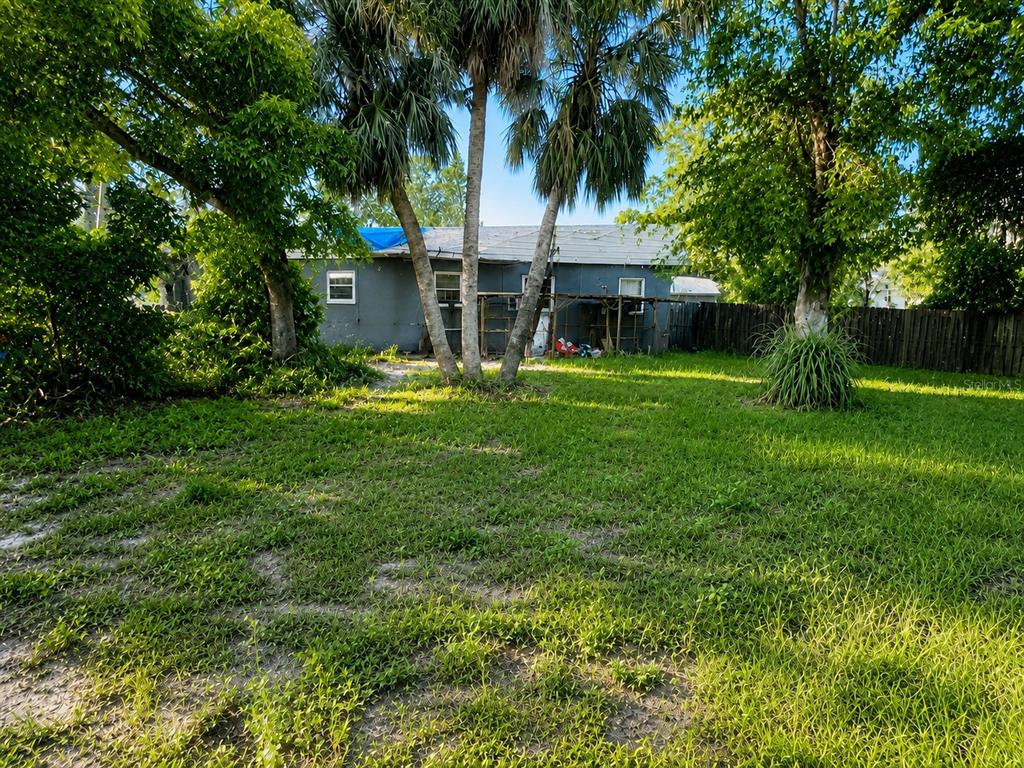 A gray house with a blue tarp on the roof sits behind a grassy yard — 1506 N MADISON AVENUE, CLEARWATER, FL