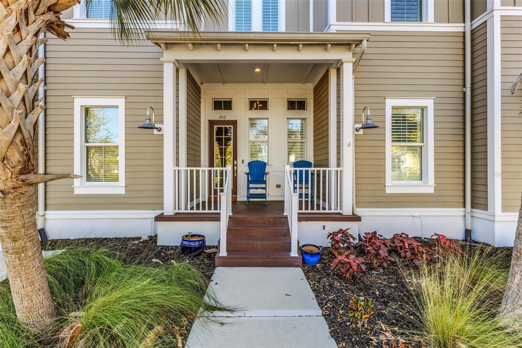 A tan-sided house exterior features a covered front porch with two blue chairs and stairs — 289 SAPPHIRE LAKE DRIVE UNIT 202, BRADENTON, FL
