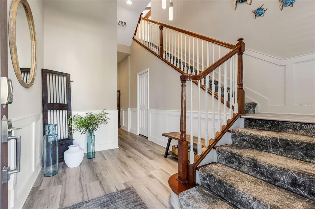 A foyer features light wood flooring, a carpeted staircase with a wooden railing, and wainscoting — 289 SAPPHIRE LAKE DRIVE UNIT 202, BRADENTON, FL