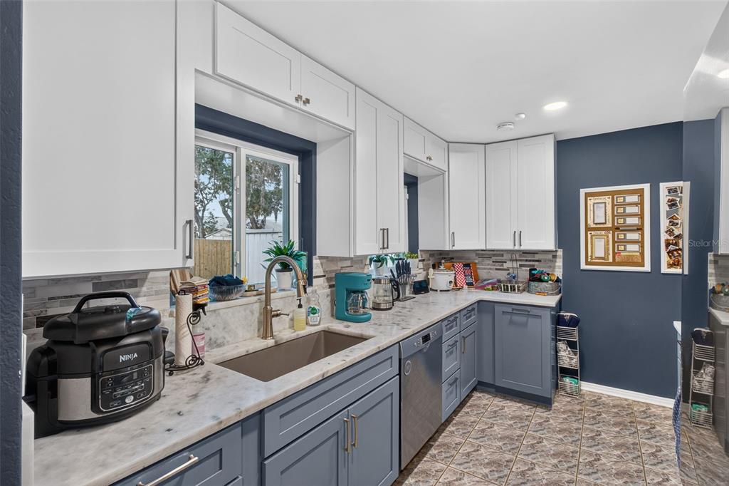 A kitchen features white upper cabinets, blue lower cabinets, marble countertops, and a farmhouse sink — 11373 67TH AVENUE, SEMINOLE, FL