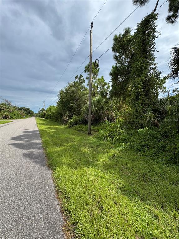 A paved road runs alongside a grassy area with dense trees and shrubs — 395 RAMBLEWOOD STREET, PORT CHARLOTTE, FL