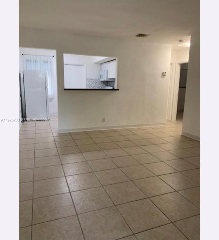 The image shows an interior living area with beige tile flooring and a kitchen pass-through window — 401 SW 8th St # A, Hallandale Beach FL 33009, HALLANDALE BEACH, FL