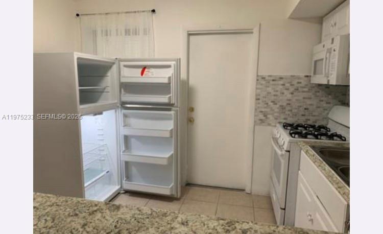 A kitchen features a white refrigerator, a gas stove, and a tiled backsplash — 401 SW 8th St # A, Hallandale Beach FL 33009, HALLANDALE BEACH, FL