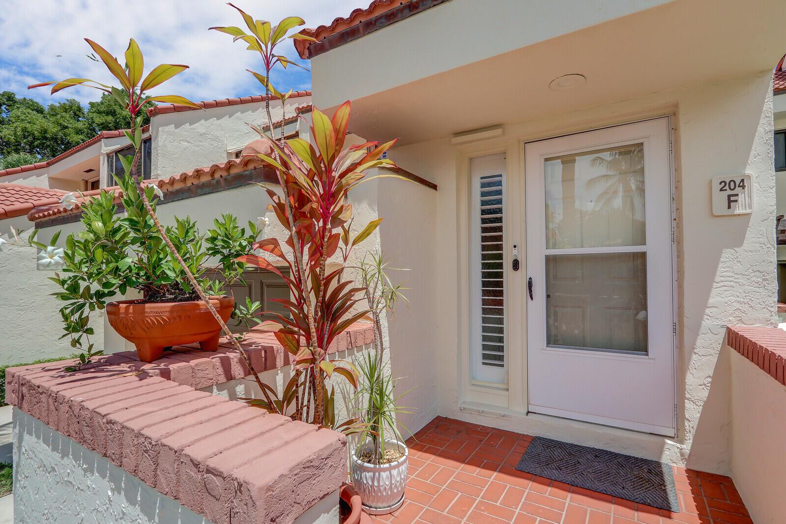 An exterior view of a residential entrance with a brick wall, potted plants, and door — 204 Sea Oats Drive # F, Juno Beach FL 33408, JUNO BEACH, FL