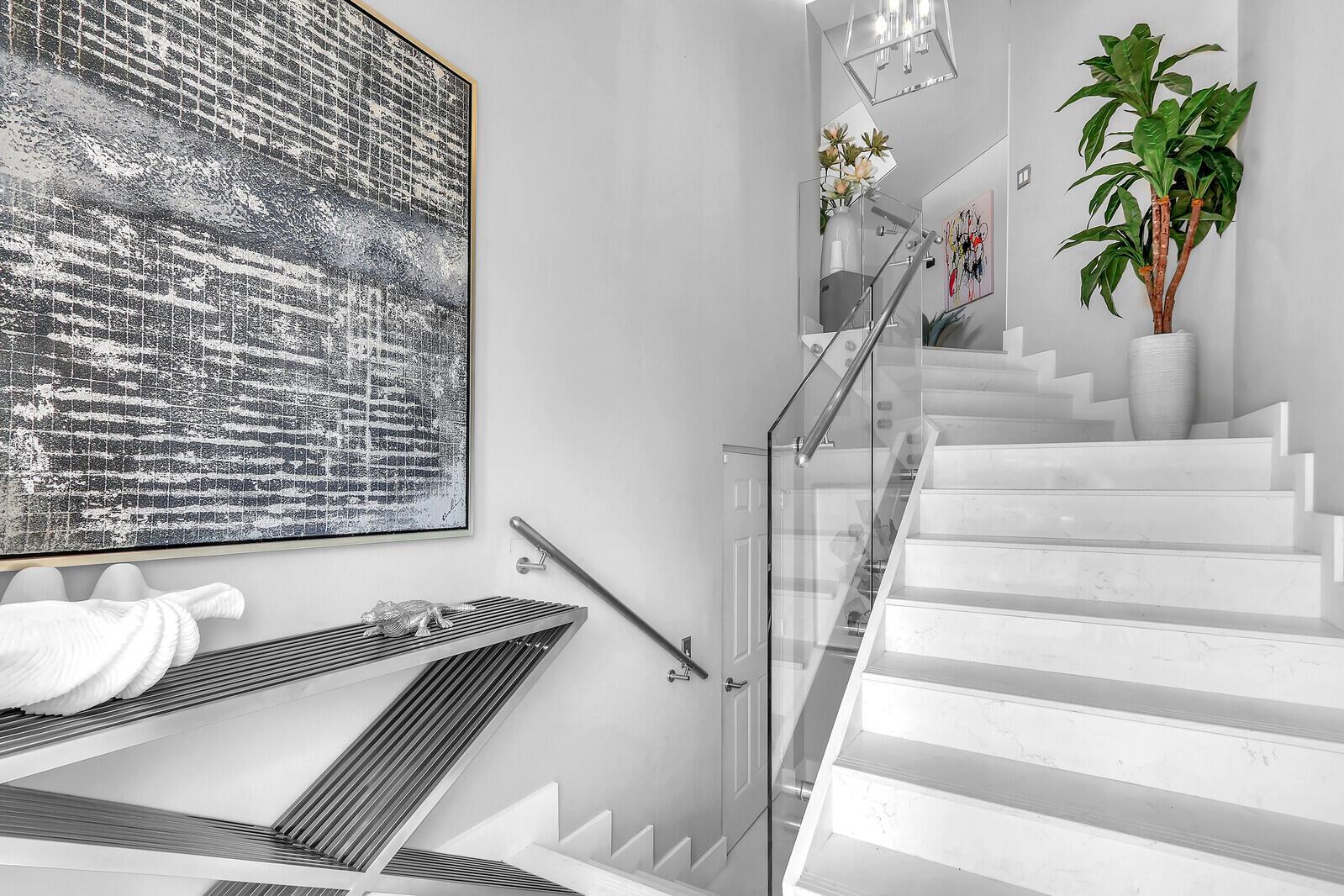 A modern staircase with white marble steps and a glass railing leads to an upper landing — 204 Sea Oats Drive # F, Juno Beach FL 33408, JUNO BEACH, FL