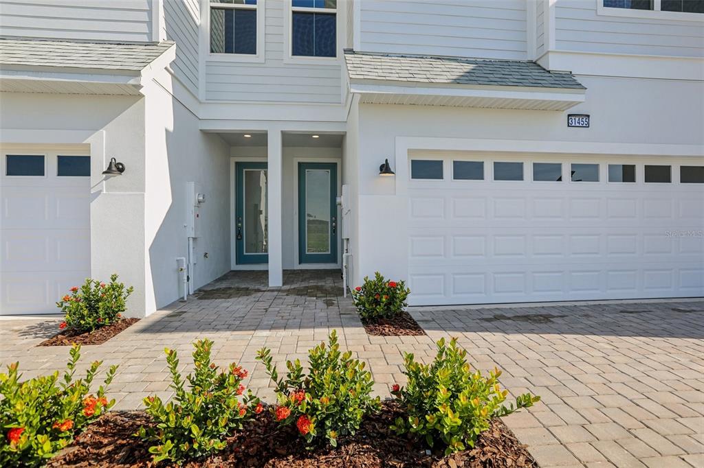 A two-story townhouse exterior features a white facade, a two-car garage, and a paved walkway — 31455 SPANISH MISSION ROAD, SAN ANTONIO, FL