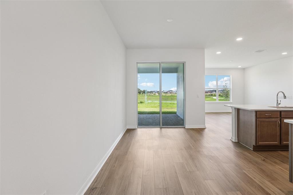 A bright room with wood-look flooring, sliding glass doors, and a partial view of a kitchen — 31455 SPANISH MISSION ROAD, SAN ANTONIO, FL
