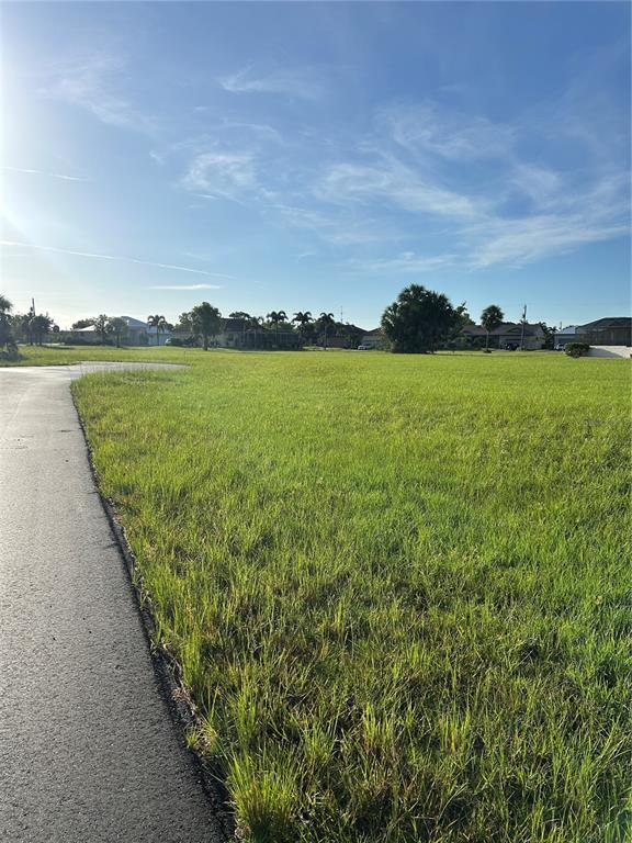 A vacant, grassy residential lot borders a paved road under a clear blue sky — 24163 COLIMA COURT, PUNTA GORDA, FL