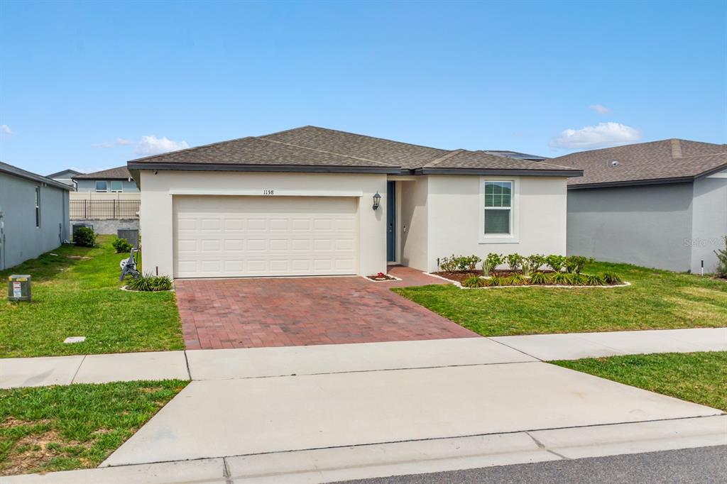 A single-story house with a beige stucco exterior, a brick driveway, and a two-car garage — 1158 FORESHORE LANE, HAINES CITY, FL