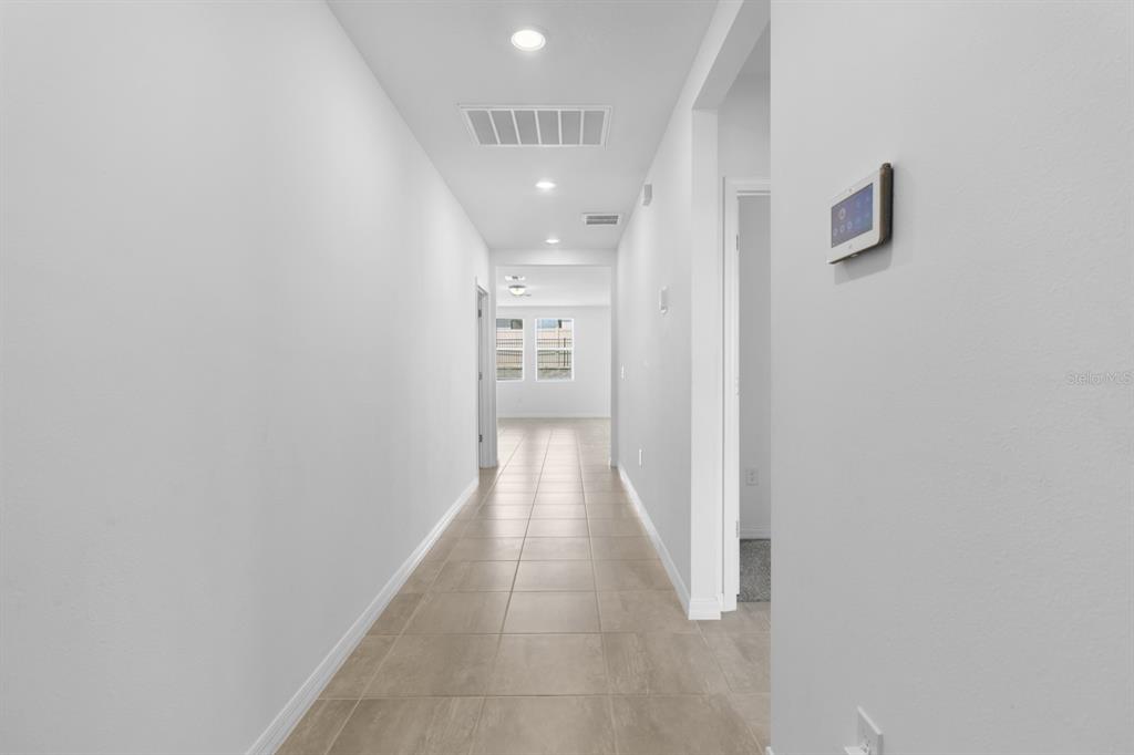 A long, tiled hallway with white walls leads toward a bright room with windows — 1158 FORESHORE LANE, HAINES CITY, FL
