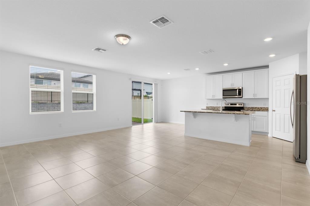 An open-concept kitchen and living area with white cabinets, granite countertops, and tile flooring — 1158 FORESHORE LANE, HAINES CITY, FL