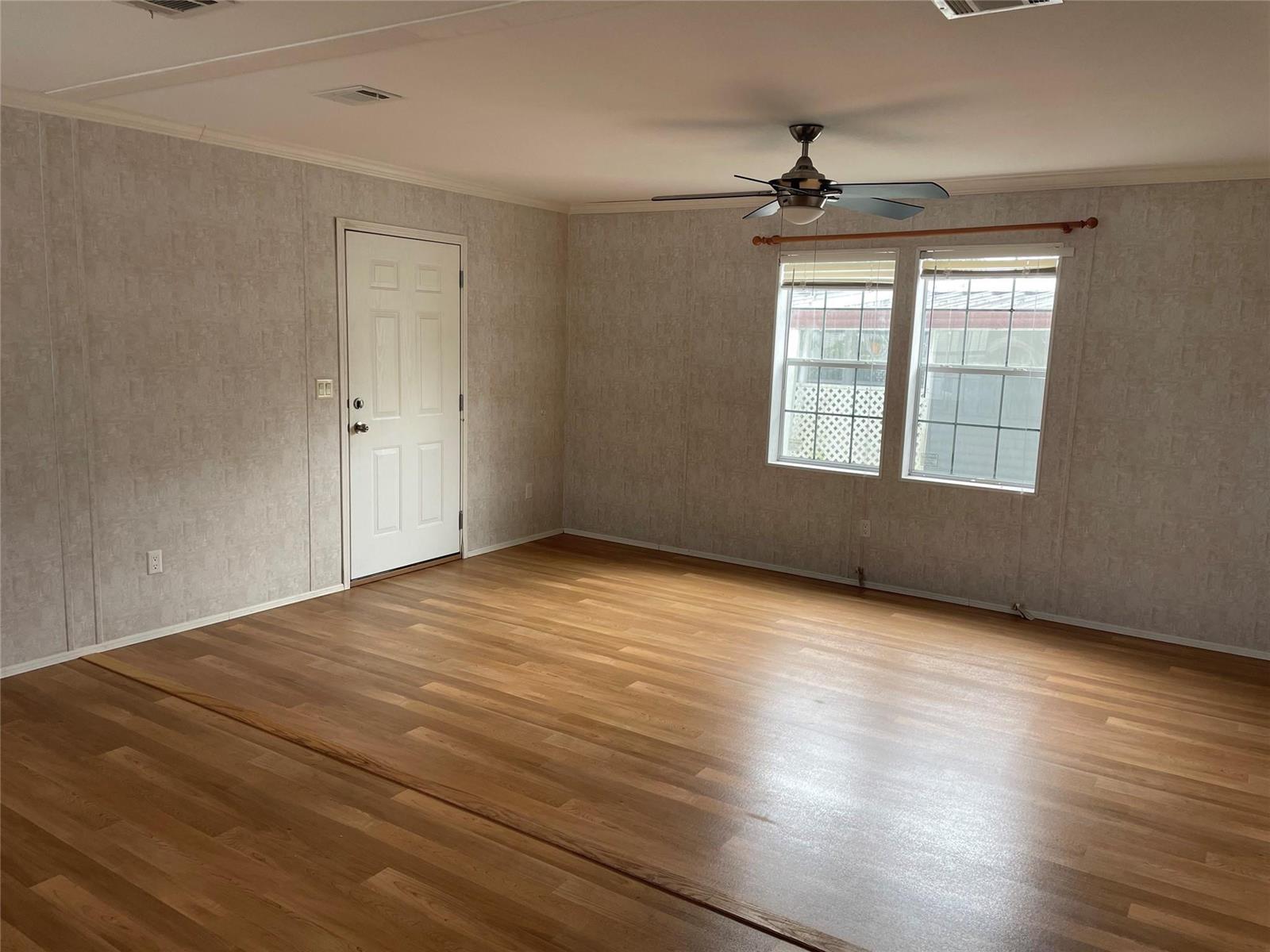 An empty living room features wood-look flooring, light-colored wallpaper, a ceiling fan, and two windows — 2321 SW 85th Avenue, Davie FL 33324, DAVIE, FL
